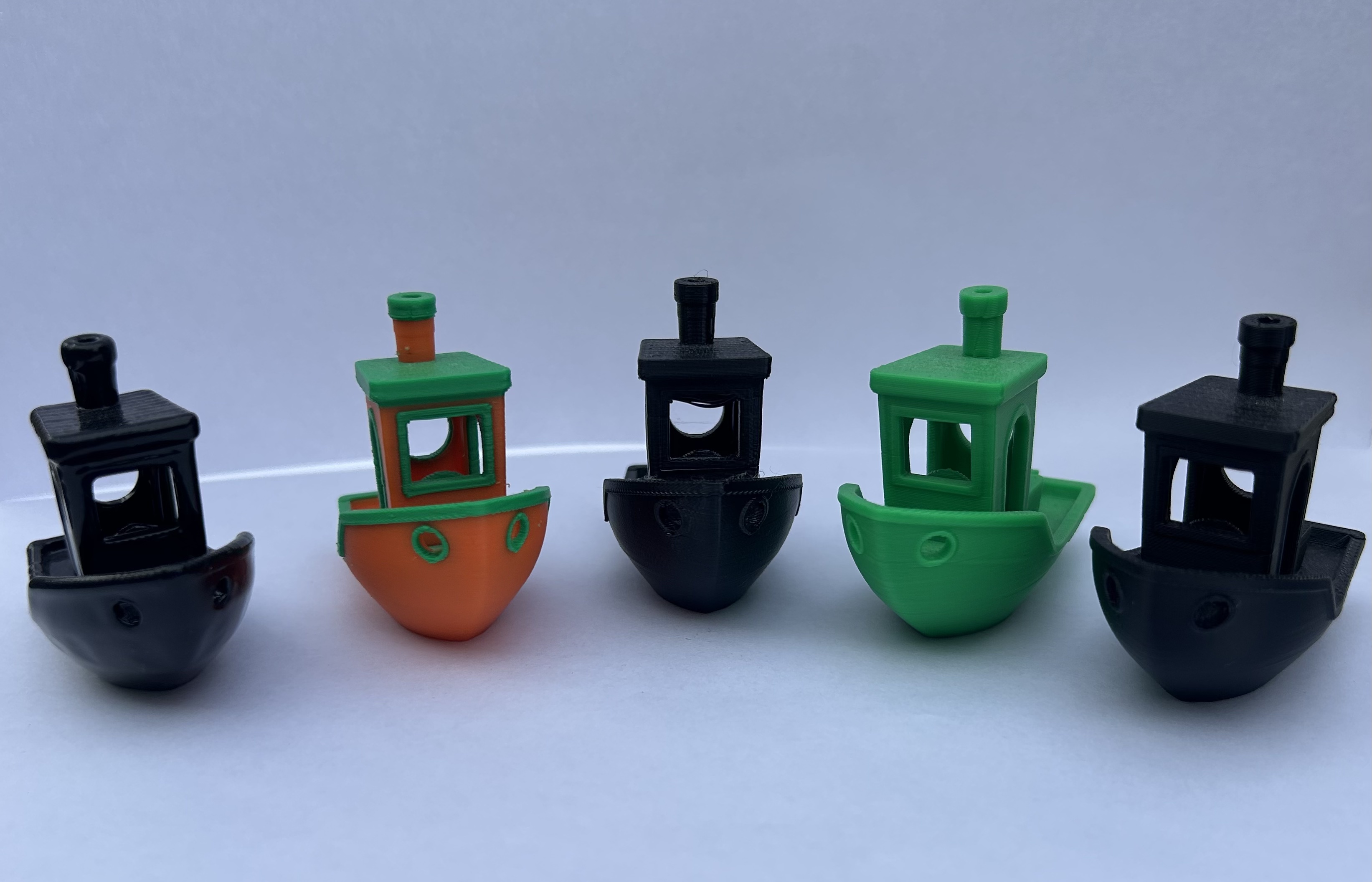 3D printed Benchy boats in black, green, and orange displayed in a row, showcasing Goin Design’s high-quality custom 3D printing and design work.